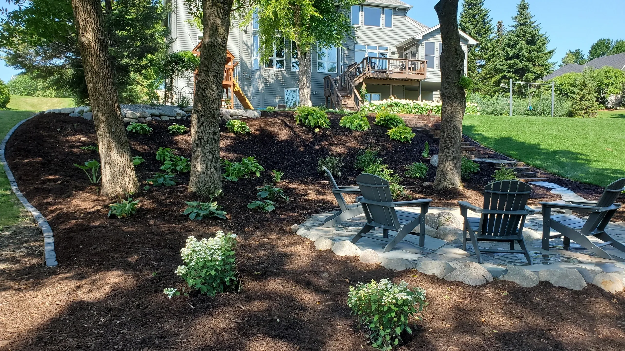 A backyard with trees, shrubs and chairs.